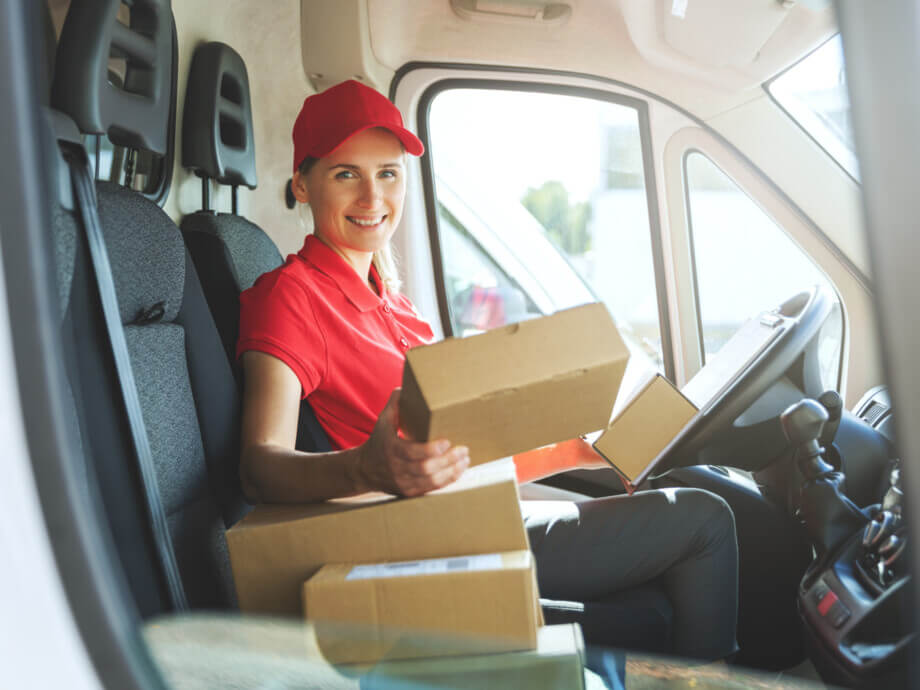 female delivery service worker in red uniform sitting in van with boxes. smiling at camera