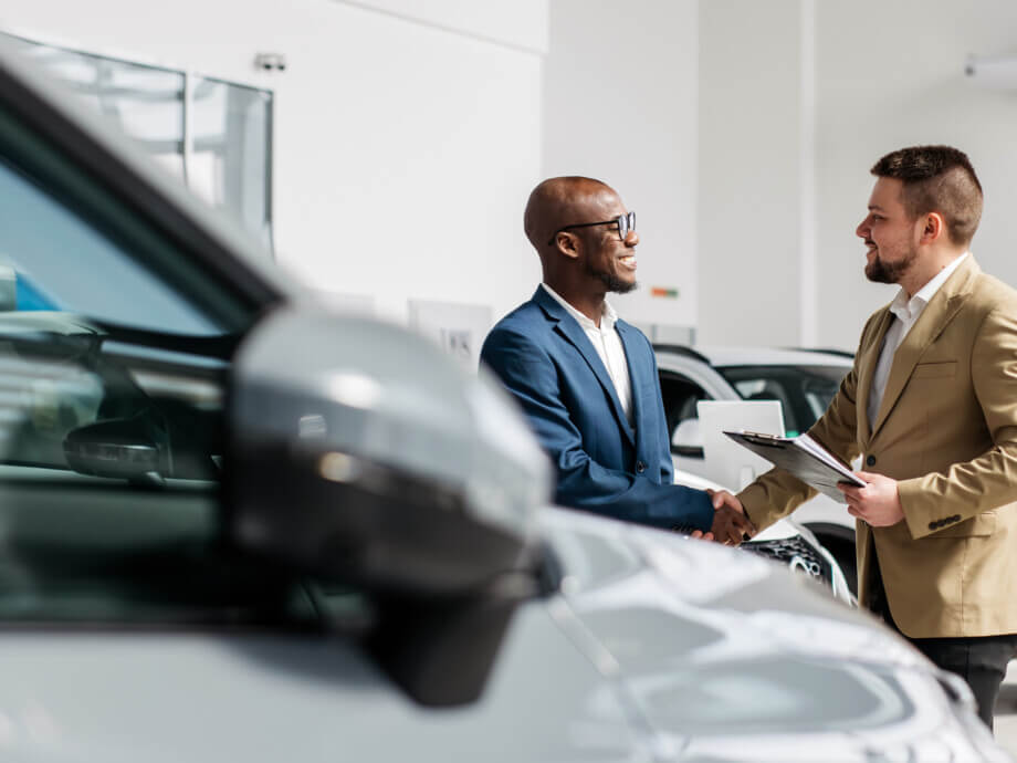 An auto dealer closes a deal or a successful consultation with a handshake with an African-American customer. The concept of successful buying and selling.